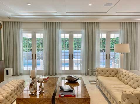 Large living room with sofas, coffee tables, and patio doors featuring ceiling to floor curtains.