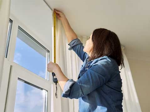 A woman taking measurements for window treatments.